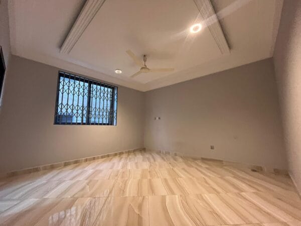 Spacious bedroom with polished marble-like tiled floors, ceiling fan, and large window with security bars.