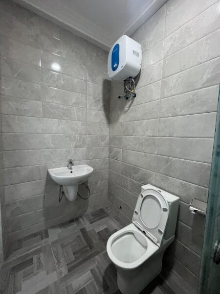 Ensuite bathroom with water heater, toilet, and sink, finished with gray and white ceramic tiles.