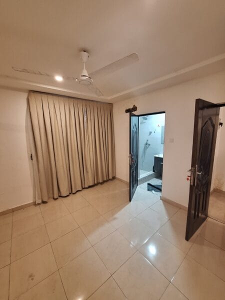 Bedroom with ceiling fan, polished tiles, beige curtains, and a doorway leading to the bathroom.