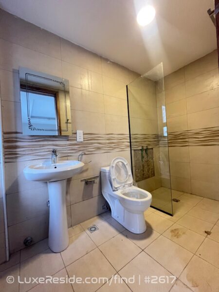 Modern bathroom with a pedestal sink, toilet, and glass-enclosed shower area, featuring beige tiles.
