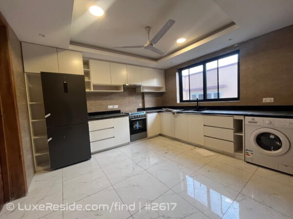 Fully fitted kitchen with sleek white cabinetry, black countertops, and built-in appliances, including a refrigerator and washing machine.