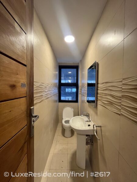 Modern bathroom with a pedestal sink, toilet, and glass-enclosed shower area, featuring beige tiles.