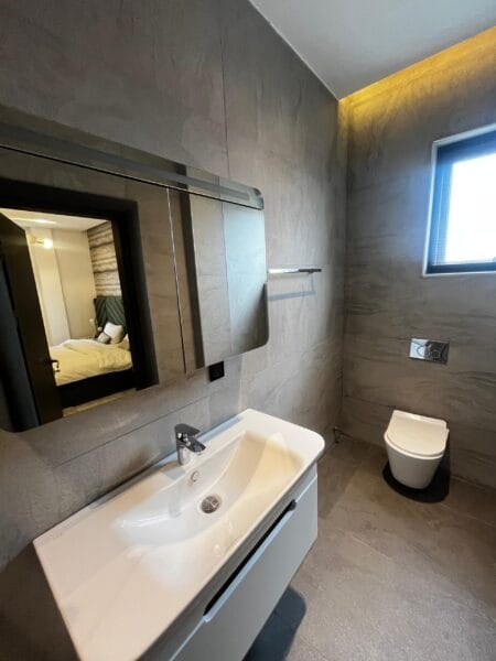 The modern bathroom includes a sleek glass shower enclosure and a stylish white sink.