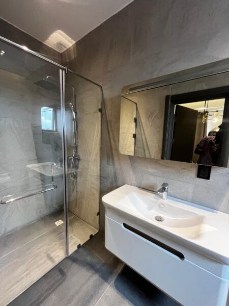 The modern bathroom includes a sleek glass shower enclosure and a stylish white sink.