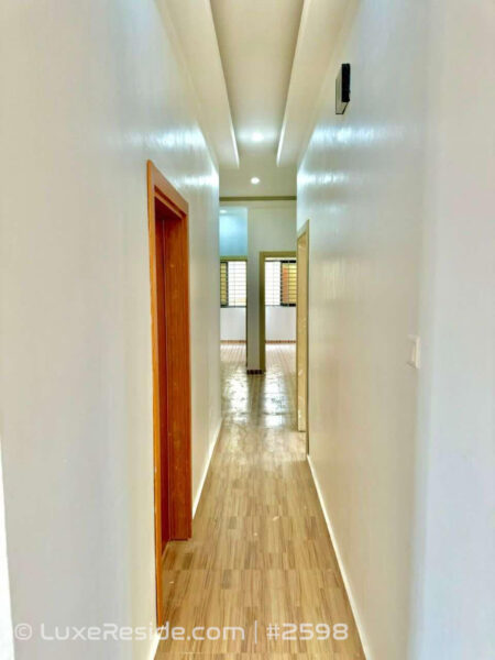 Long, bright interior hallway with wooden doors, stylish flooring, and ceiling lights.