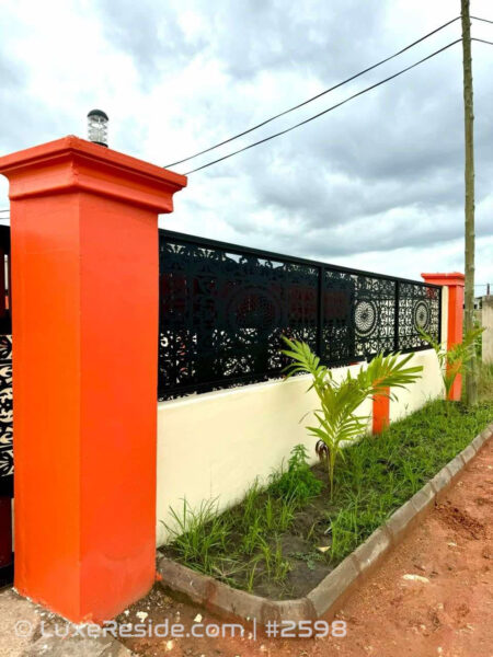 Modern perimeter wall with orange pillars, decorative metal fencing, and landscaped plants.
