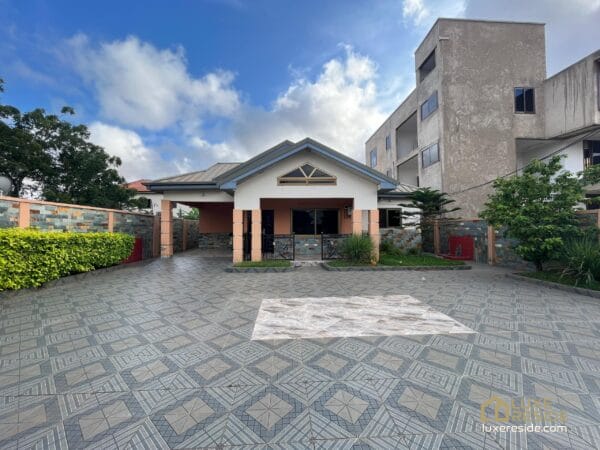 Spacious paved compound with lush green hedges and the exterior view of the house.