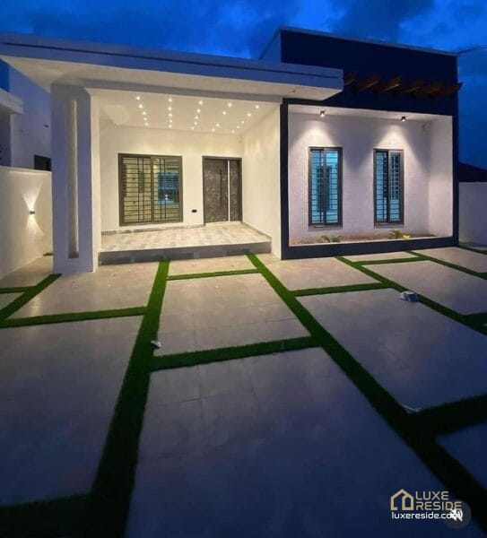 Well-lit front yard with a modern façade and tiled driveway at night.