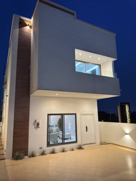 Front elevation of a 3-bedroom self-compound house in Ayi Mensah featuring paved driveway, garden area, and gated entrance.