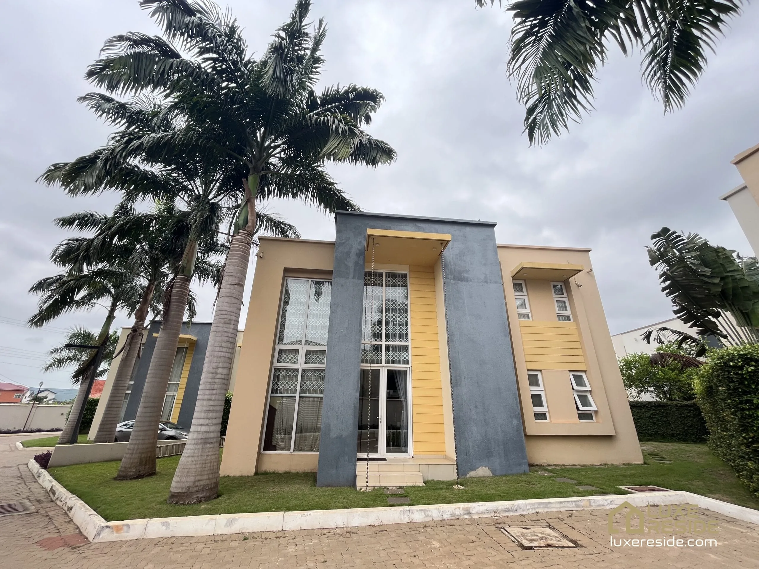 Exterior of modern 3-bedroom townhouse in Adjiringanor, with palm trees and neat landscaping.