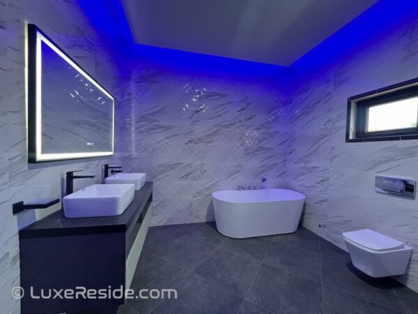 Luxurious bathroom with marble walls, a soaking tub, and LED mirror